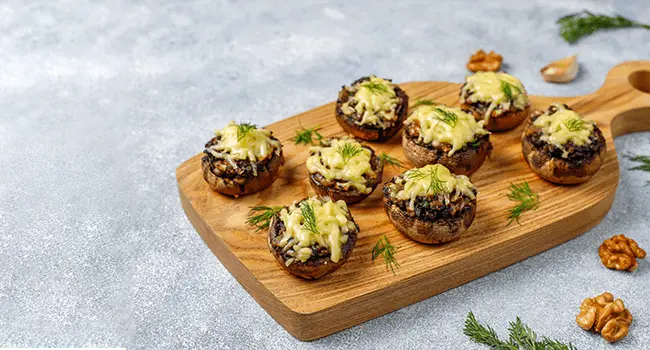 Bocaditos de champiñones, un aperitivo presentados en una tabla con agarradera sobre una mesa gris