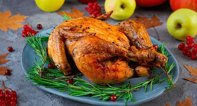 Pollo entero asado con hierbas con frutas alrededor