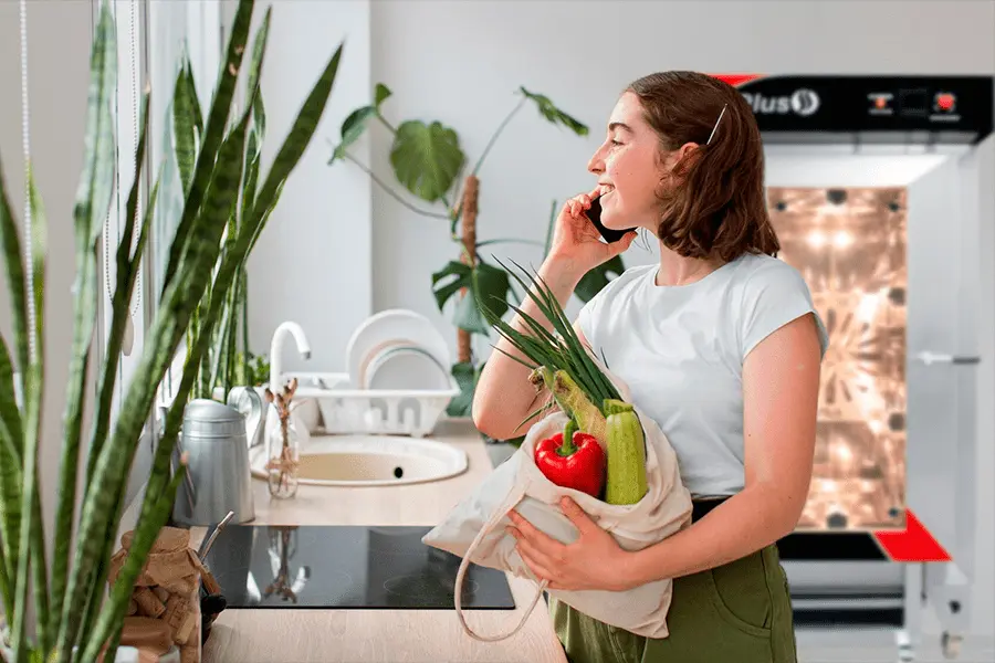 Adolescente sosteniendo una bolsa con algunos vegetales en una cocina ecologica con un horno de convección al fondo