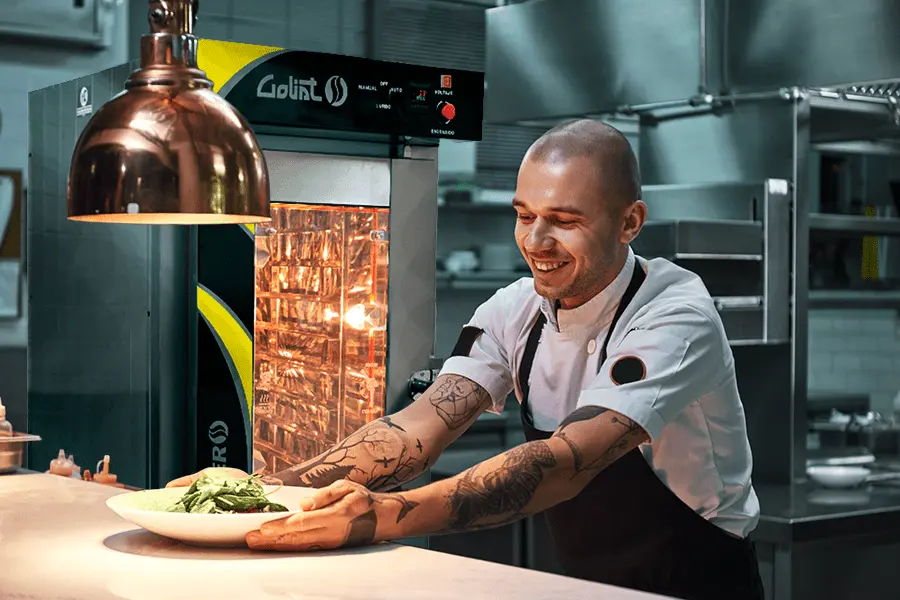Chef sirviendo un platillo en la cocina de un restaurante con un horno de convección al fondo