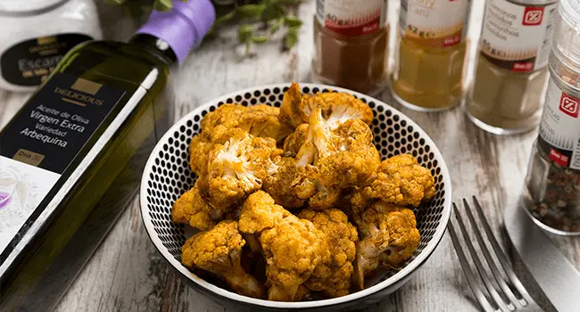 Coliflor asada con especias servida en un plato con varios condimentos a su alrededor