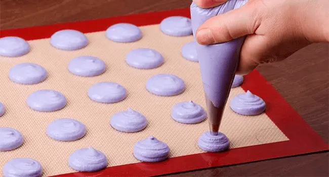 Mano de mujer repostera colocando una mezcla para crear macarons sobre un tapete de silicona