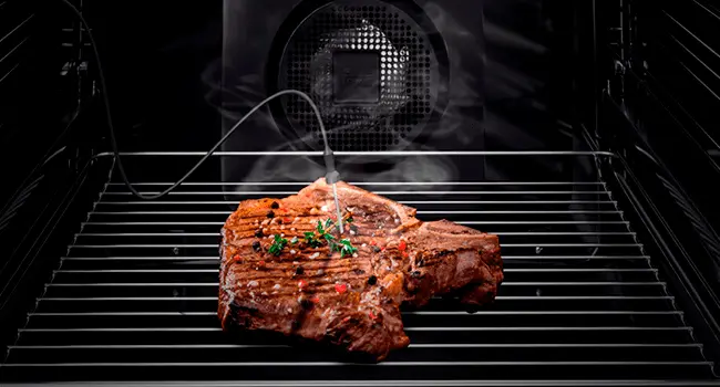 Vista interior de un horno de convección con un trozo de carne dentro y una sonda de temperatura