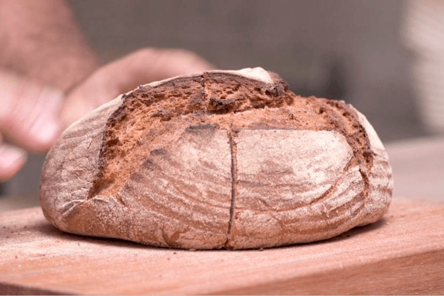 Manos de panadero a punto de tocar un pan de campo tradicional en una tabla de cortar