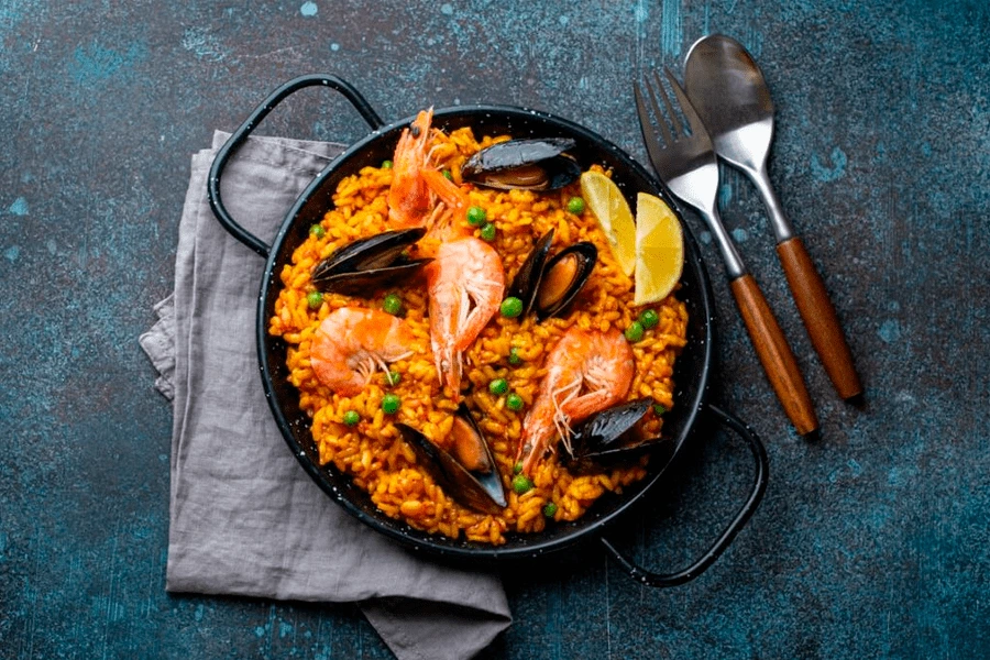Olla con paella con algunos cubiertos en una mesa