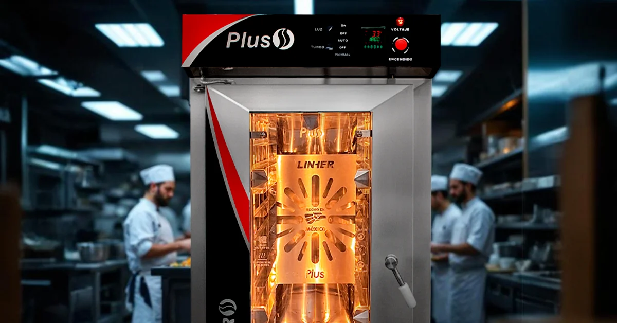 Horno de convección industrial funcionando en cocina escolar, con bandejas de comida saludable y equipo de cocina trabajando al fondo.