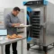 Horno de convección industrial LINHER Essential en una cocina profesional moderna, con charolas alineadas y preparaciones de prueba, mostrando innovación, control y desarrollo técnico gastronómico.